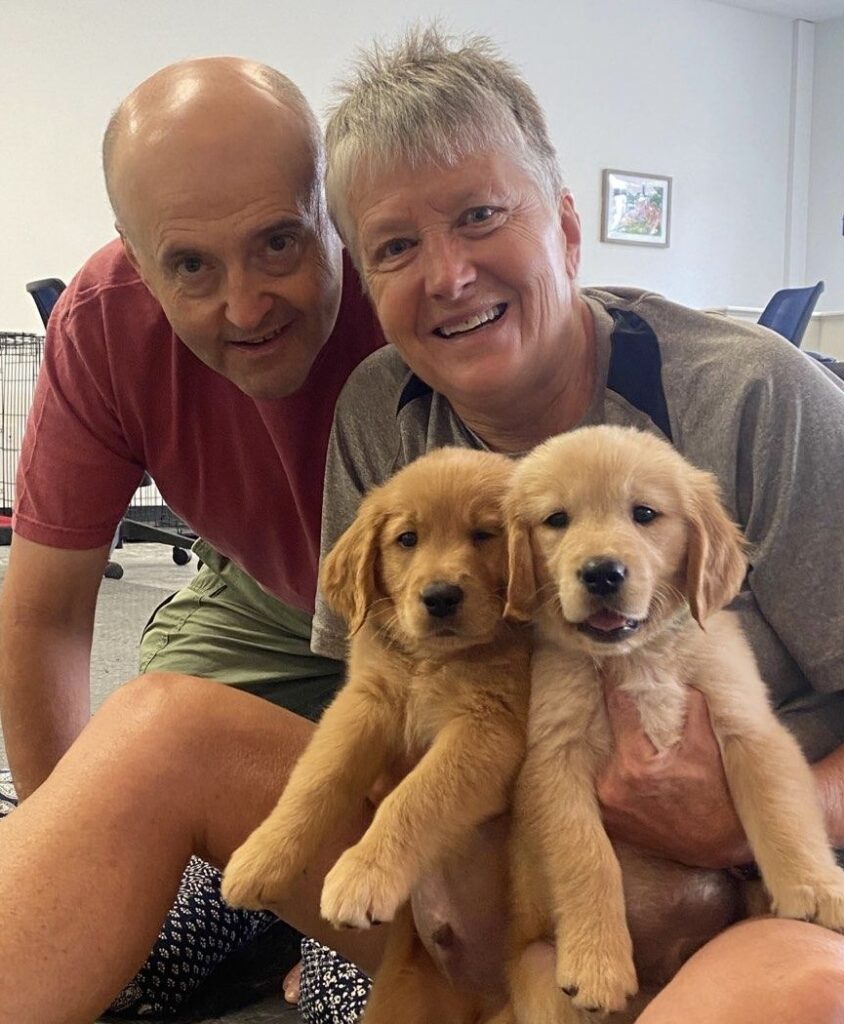 man and woman hold two golden retriever puppies