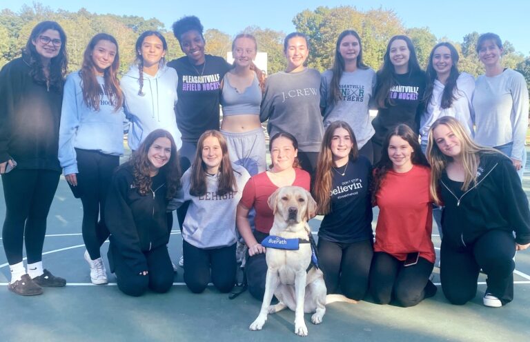 Girls field hockey team poses with yellow Labrador retriever